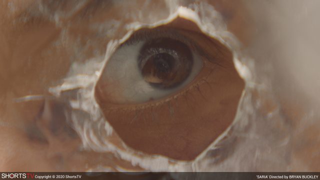 Ein Auge schaut durch ein Loch in einer Scheibe aus dem Kurzfilm Saria. Oscar Nominierter Kurzfilm