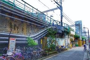Die Brücke am Shinjuku O-Guard im gleichnamigen Stadtviertel Shinjuku und wurde für WEATHERING WITH YOU fast 1:1 nachgezeichnet, sogar Details wie die Wandbemalung oder die schwarz-gelb gestreiften Pfeiler lassen sich am Originalschauplatz finden.