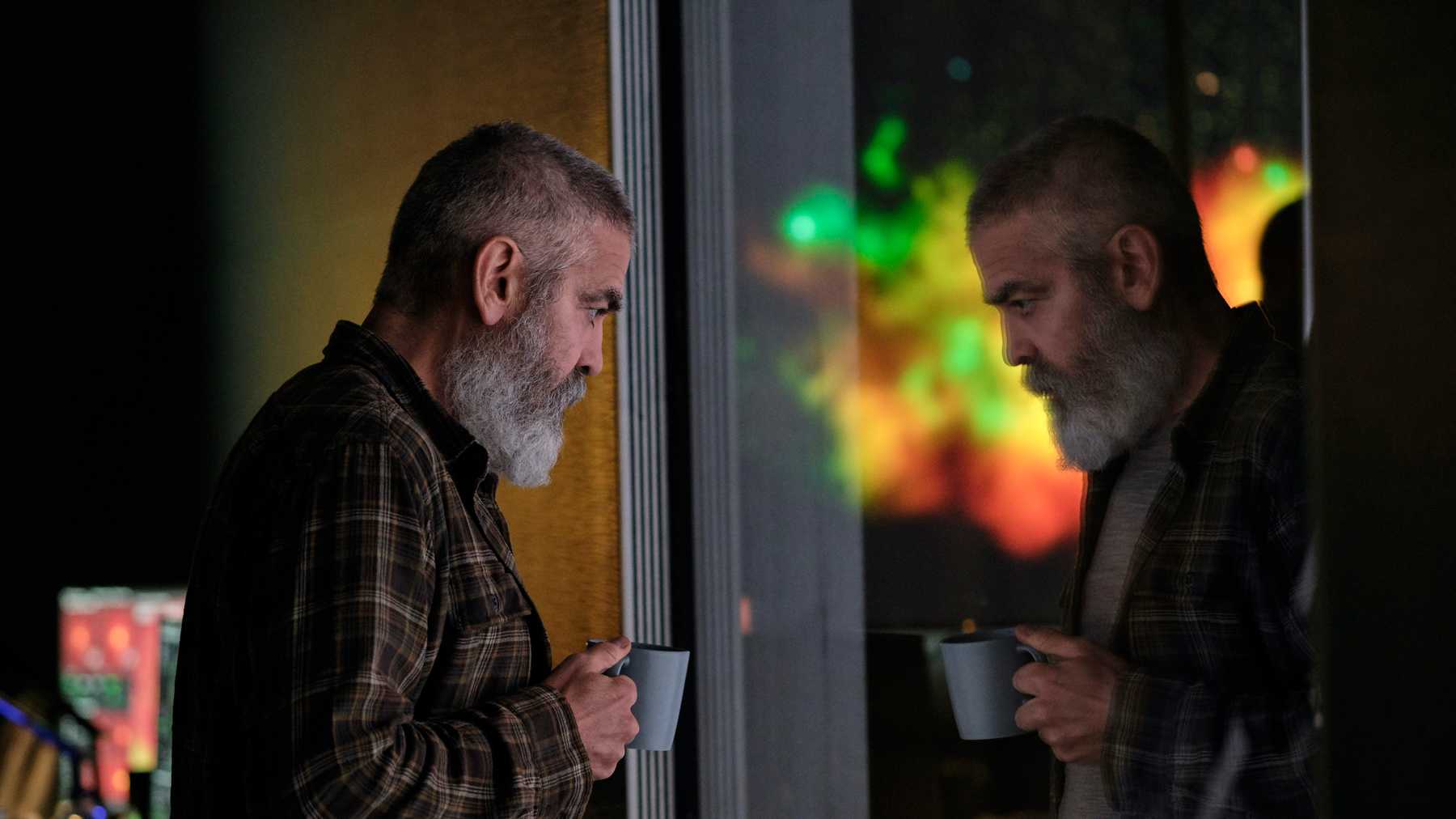George Clooney mit Vollbart am Fenster mit einer Tasse in seiner hand. Er schaut nachdenklich in seinem neuen Film The Midnight Sky, der ab Dezember bei Netflix zu sehen ist.