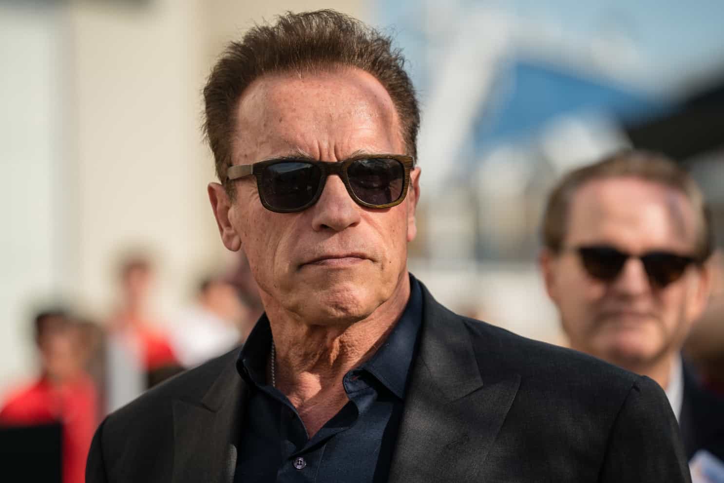 Arnold Schwarzenegger mit Sonnenbrille und im Anzug bei einer Premierenfeier