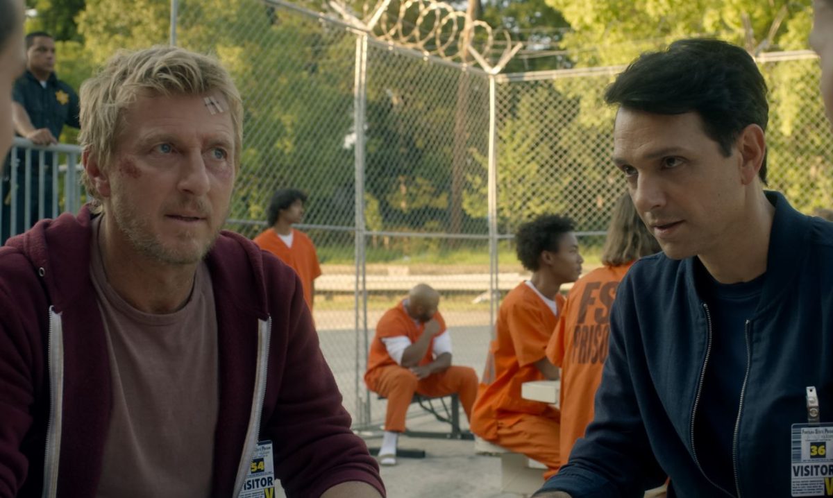 Ralph Macchio u William Zapka sitzen an einem Tisch mit Gefängnisinsassen. Szene aus der Serie Cobra Kai auf Netflix
