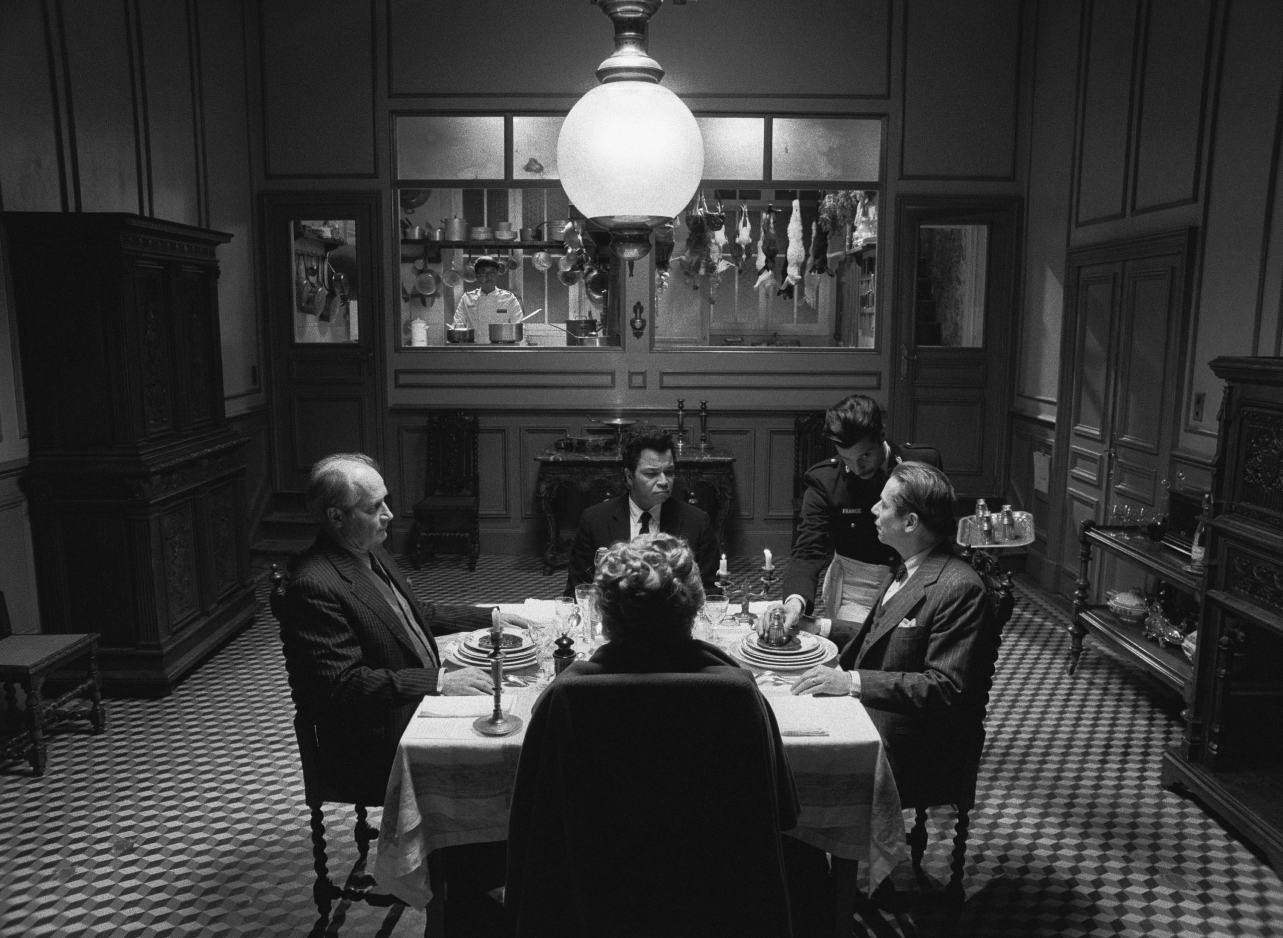 Vier Personen sitzen um einen T isch herum und essen. Eine Person bedient. Eine Szene aus dem film The French Dispatch