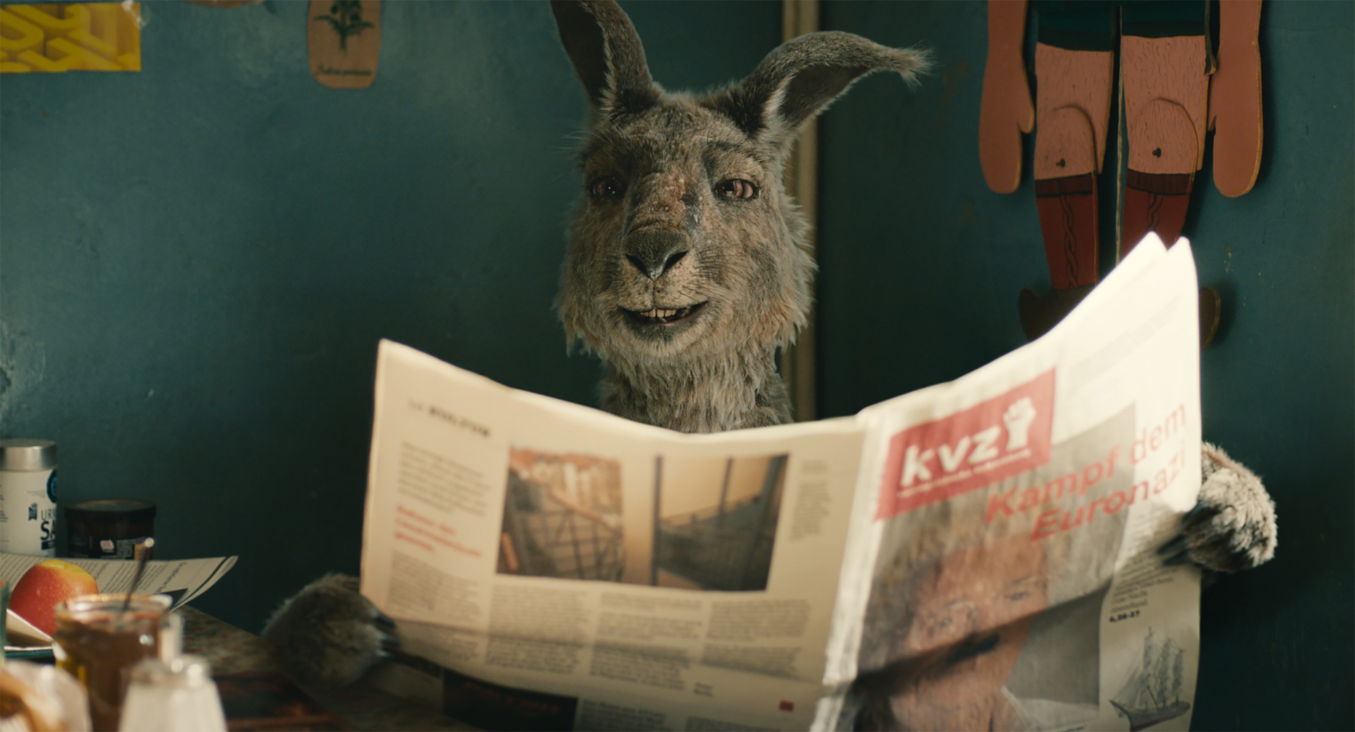 "Die Känguru-Chroniken": Das Känguru sitzt am Küchentisch mit einer Zeitung in der Hand und grinst in Richtung Kamera.