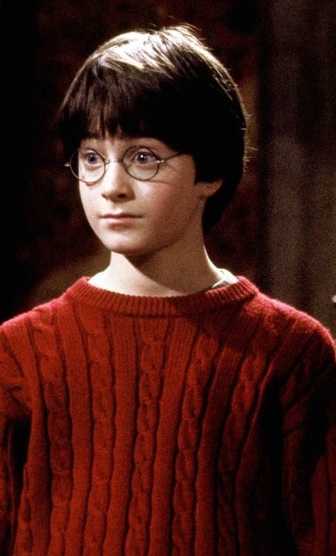 Daniel Radcliff als Harry Potter aus der Stein der Weisen. TRägt einen roten Pullover und eine Brille