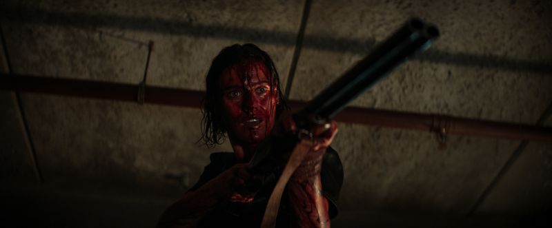 Eine Frau mit blutverschmierten Gesicht und einem Gewehr im Anschlag aus dem Film Evil Dead Rise