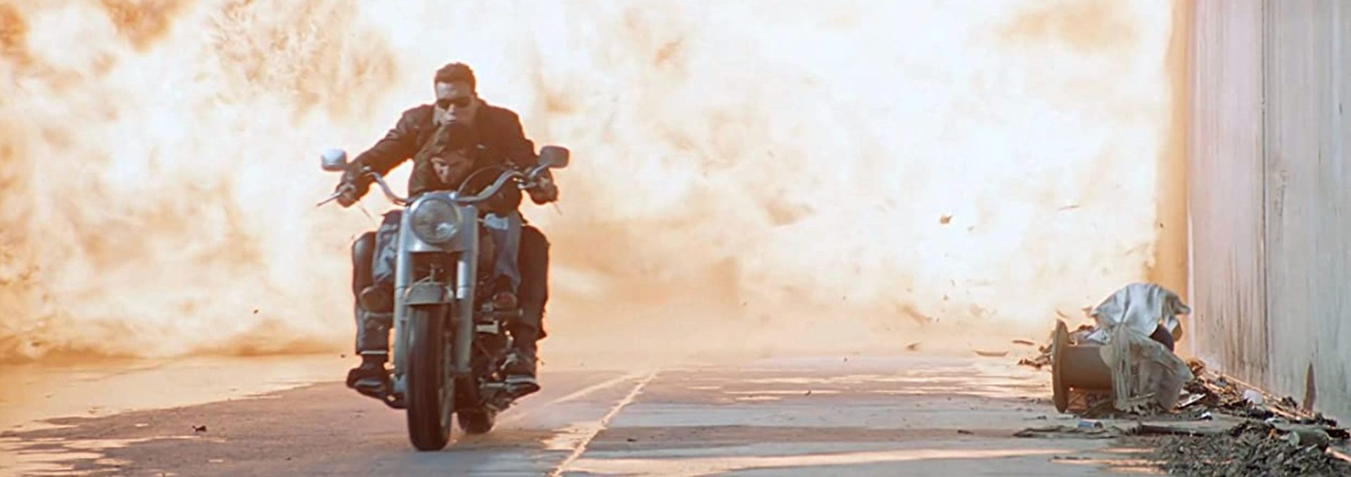 Arnold Schwarzenegger als TERMINATOR mit Edward Furlong auf einem Motorrad. Hinter ihnen ein Flammenmeer.