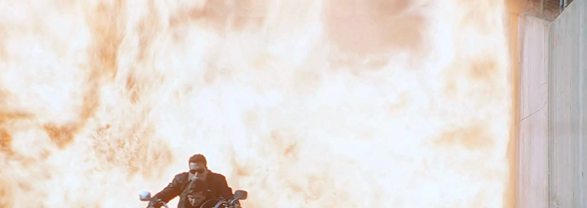 Arnold Schwarzenegger als TERMINATOR mit Edward Furlong auf einem Motorrad. Hinter ihnen ein Flammenmeer.