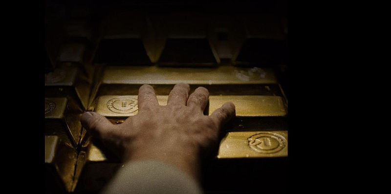 EINE HAND GREIFT NACH GOLDBARREN IM FILM THE WEIGHT - IM GOLDRAUSCH